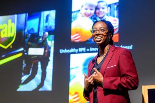 Sydney Williams speaks on stage in front of screen